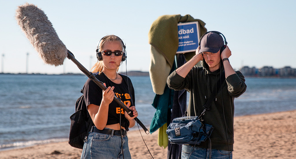 Två personer på stranden med ljudutrustning