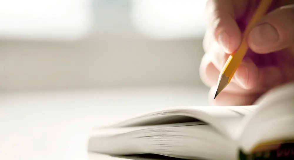 Närbild på hand som håller blyertspenna och skriver i anteckningsbok.